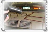 A person is using a vacuum to clean the air conditioning vents in a car.
